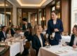 Servicemitarbeiterin präsentiert Gästen eine Weinflasche im eleganten Restaurant mit weiß eingedeckten Tischen