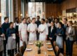 Gruppe aus Köchen, Servicekräften und Management steht gemeinsam an einer eingedeckten Tafel im Restaurant