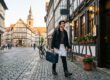 Junger Koch mit Messerkoffer geht durch eine Fachwerk-Altstadt mit Kopfsteinpflaster