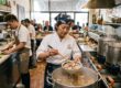 Köchin schöpft Suppe aus einem großen Topf in einer asiatischen Restaurantküche mit Dampfkörben